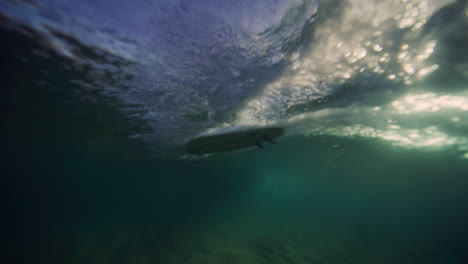 Sparkling-light-illuminates-surfer-with-arms-up,-view-from-below-clear-water-surface