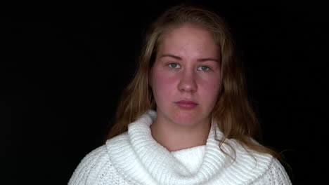 sad young woman on a black background looks at the camera