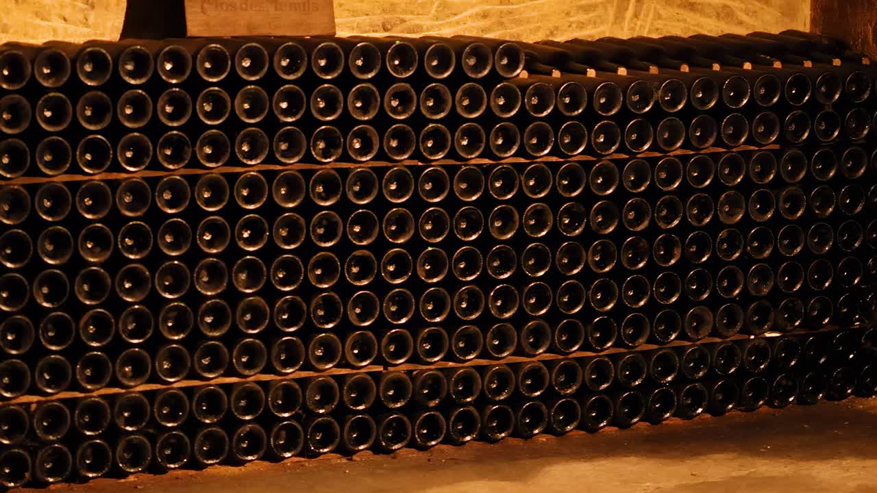 Neatly stacked wine bottles in a dimly lit, stone-walled cellar corner.