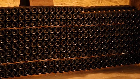 neatly stacked wine bottles in a dimly lit, stone-walled cellar corner.