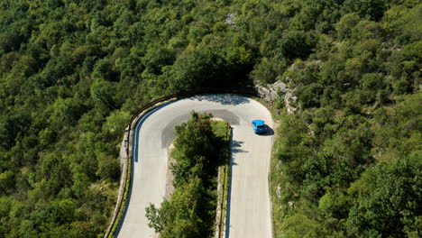 Blue-Car-Slowing-Down-On-Downhill-Curve-Road-Through-Green-Mountain-In-Istria,-Croatia