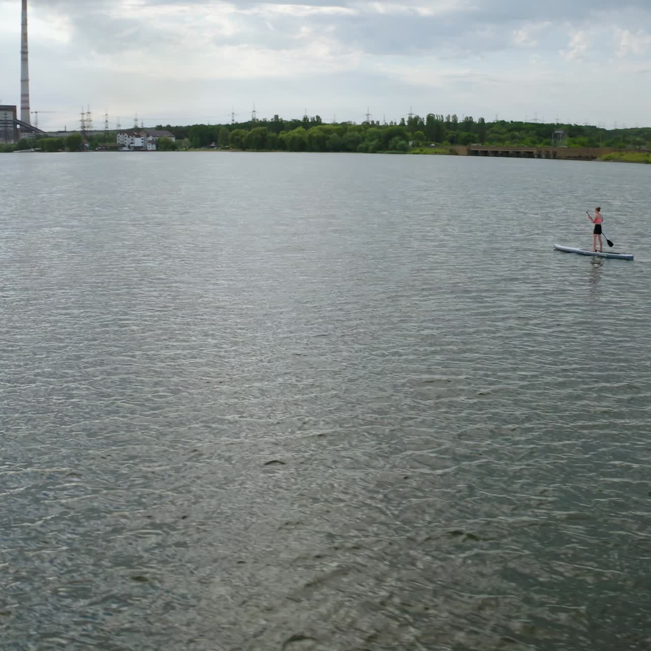 Young people sailing on water. Man and woman travelling on river on paddle boards on industry background in the evening. Summer rest