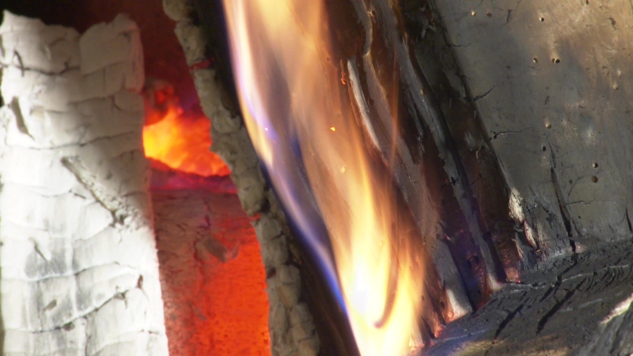Primo piano in time-lapse di braci ardenti, cenere e legna carbonizzata che cambiano lentamente all'interno di un caldo camino rustico di casa.