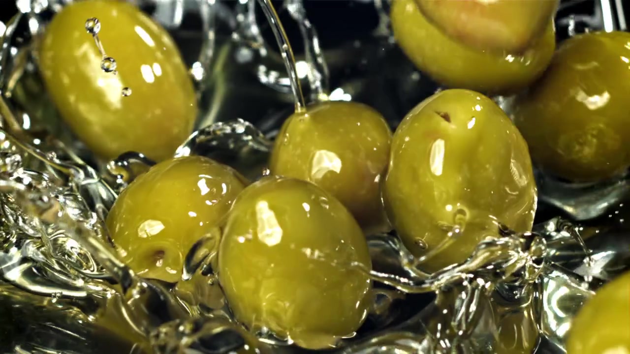 Olive verdi che cadono in un liquido al rallentatore