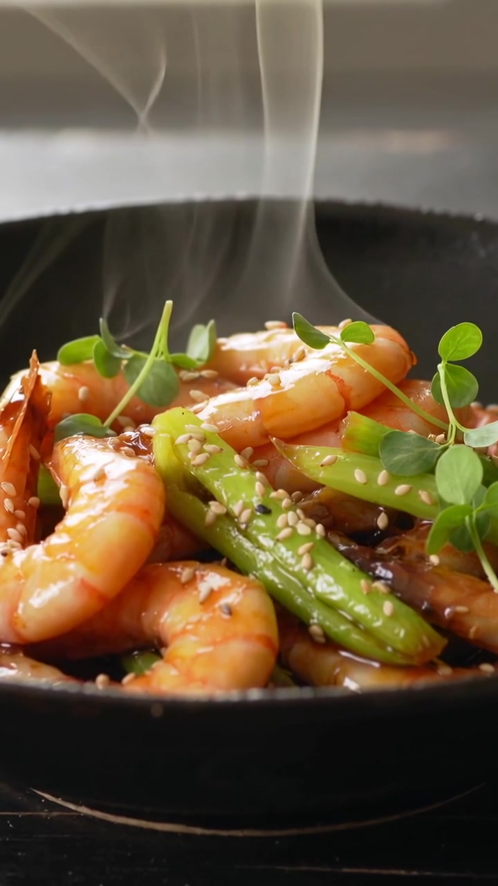 Vertical video: Releasing cooked shrimp in black pan steaming from heat in kitchen with microherbs