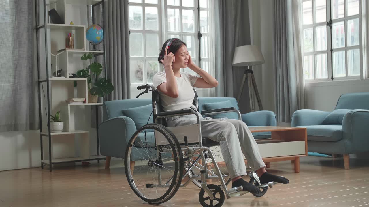 Asian Woman Sitting In A Wheelchair Listening To Music With Headphones In Living Room
