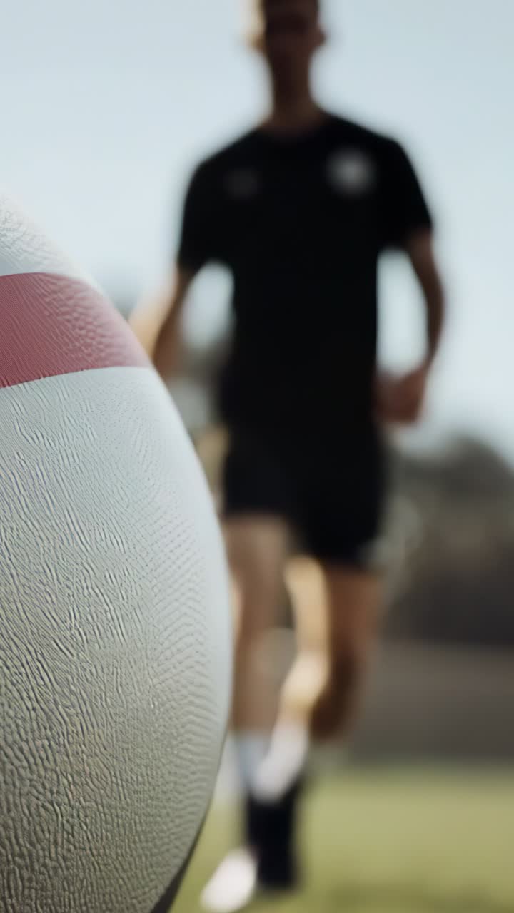 Vertical video: Jogging athlete noticing ball and closing gap toward ball on field, with goalpost