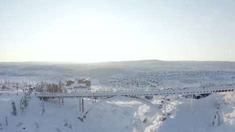 Drone-shot-of-a-big-frozen-bridge-with-a-lot-of-snow-on-it-during-a-cold-winter-sunset-at-Branäs,-Sweden