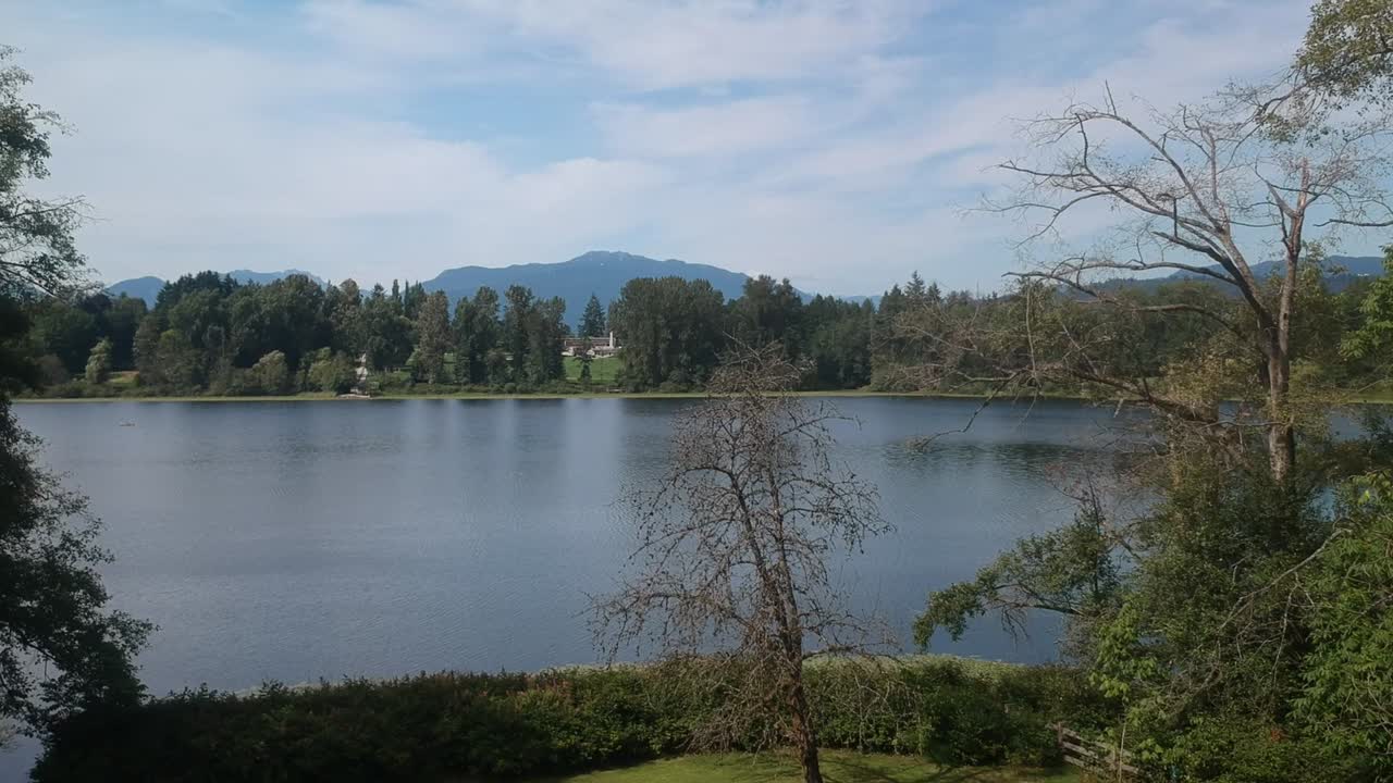 volar sobre el estanque del lago del bosque del parque con exuberantes árboles verdes césped con montañas circundantes en una comunidad del valle en un día de verano con aguas tranquilas y planas con cielos azules y nubes parciales