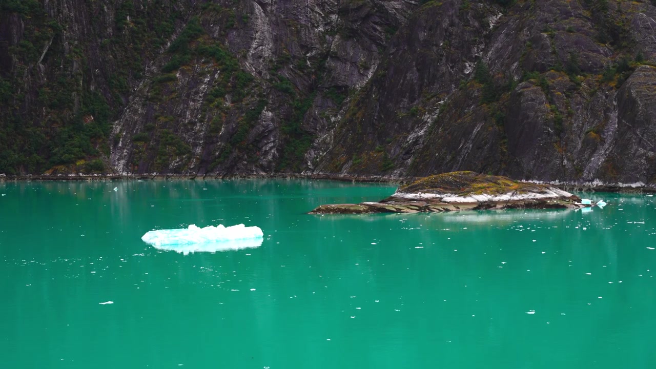 Acqua turchese brillante del fiordo con un piccolo iceberg alla deriva vicino a una costa rocciosa e muschiosa in Alaska, Canada