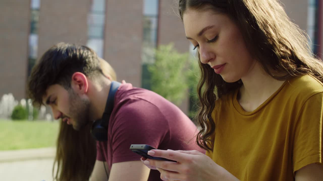chica caucásica navegando por teléfono junto a un grupo de otros estudiantes
