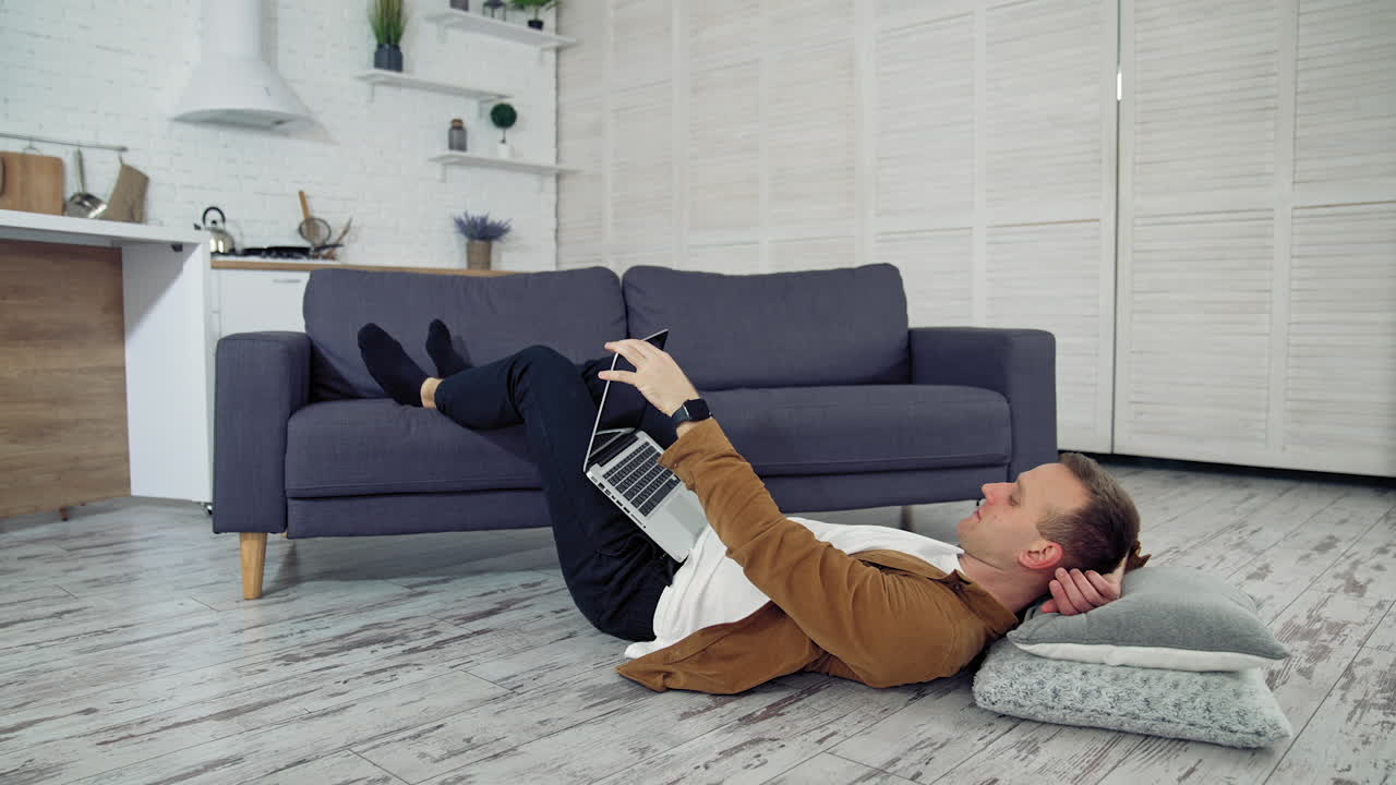 Freelancer works on laptop on floor. Tired young businessman lying on a floor and puts aside the laptop after the long job at home. Distant job during quarantine.