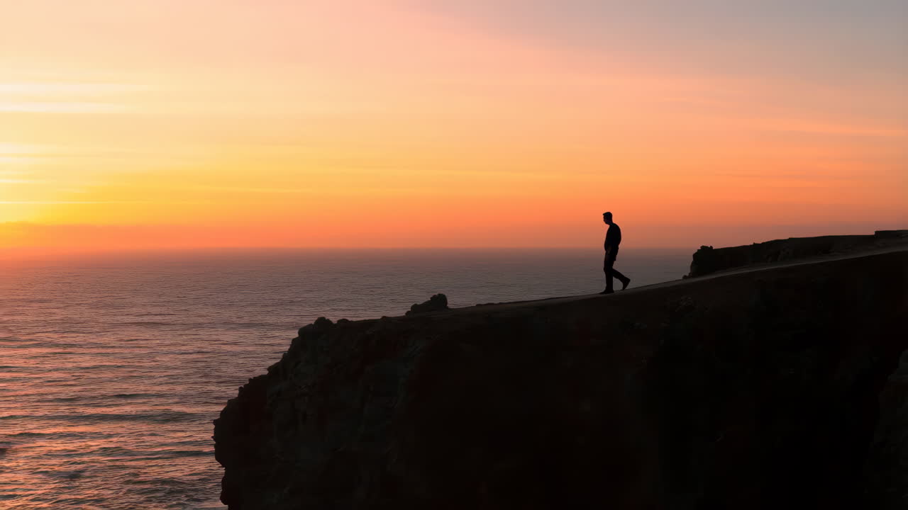 Silhouette di una persona che cammina sul bordo di una scogliera al tramonto