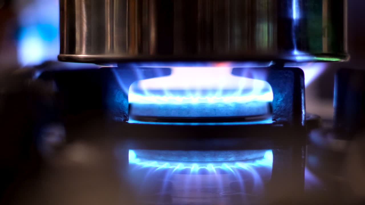 Telephoto view of blue flame of gas stove burning under stainless steel pot
