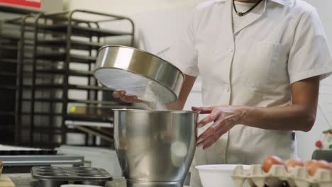 Baker-sieving-flour-into-bowl-in-kitchen