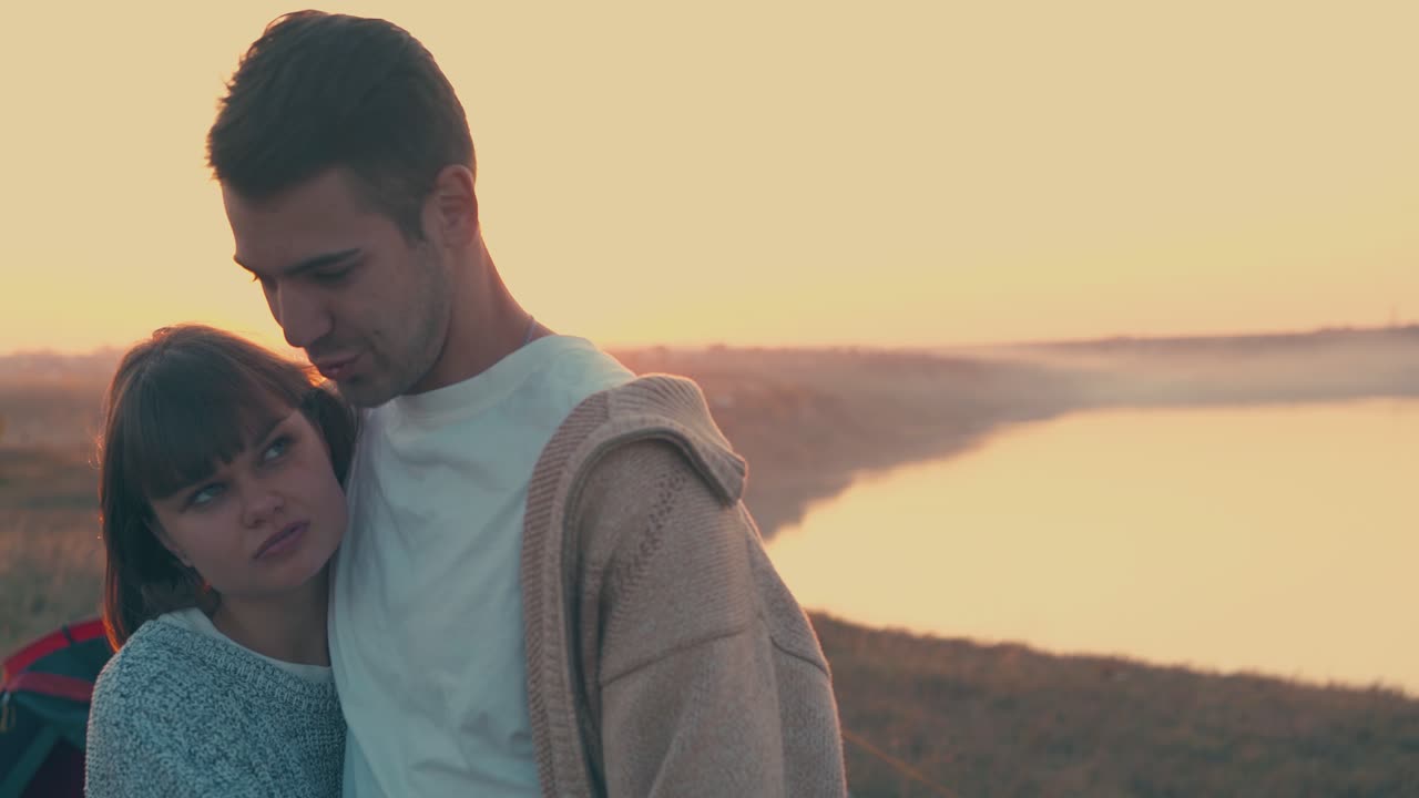 feliz pareja abrazos en el campamento turístico en la orilla del río al atardecer