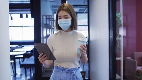 asian businesswoman wearing mask walking using digital tablet in modern office