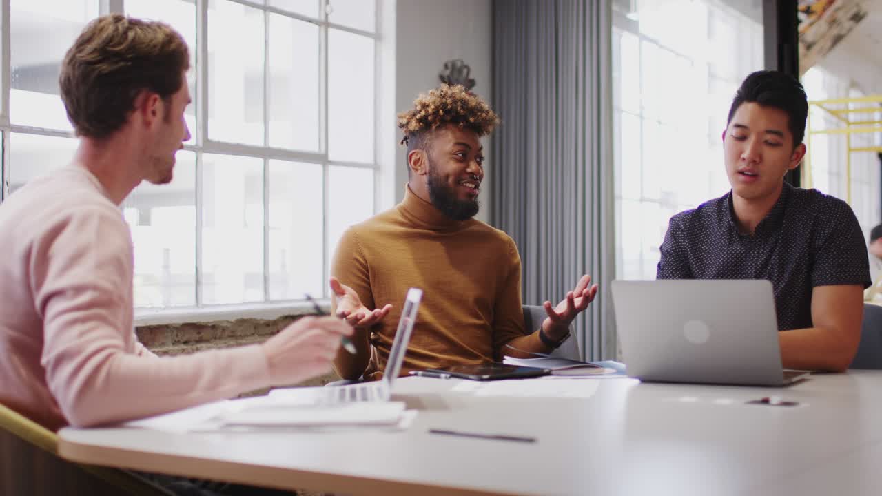 Young male creative business team working together in an office meeting room, close up, low angle