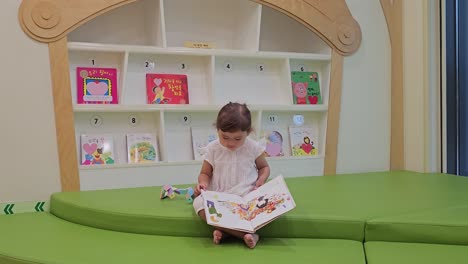niña rubia de 3 años leyendo y girando páginas con imágenes de libros infantiles - gran ángulo