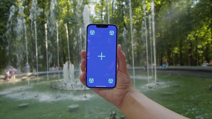 Giovane donna che tiene un telefono con schermo chroma key nel parco davanti a una fontana, primo piano. Ragazza con schermo verde su smartphone. Natura