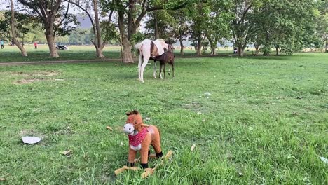 a toy horse standing near a original horse and his child in a park