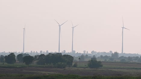 Las-Turbinas-Eólicas-Giran-Por-La-Tarde-Mientras-Las-Tierras-De-Cultivo-Con-árboles-Crean-Una-Hermosa-Silueta-De-Un-Paisaje-Y-Un-Cuervo-Vuela-De-Izquierda-A-Derecha