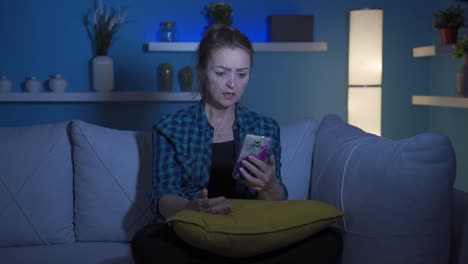 la mujer que envía mensajes de texto en el teléfono en casa por la noche está decepcionada.