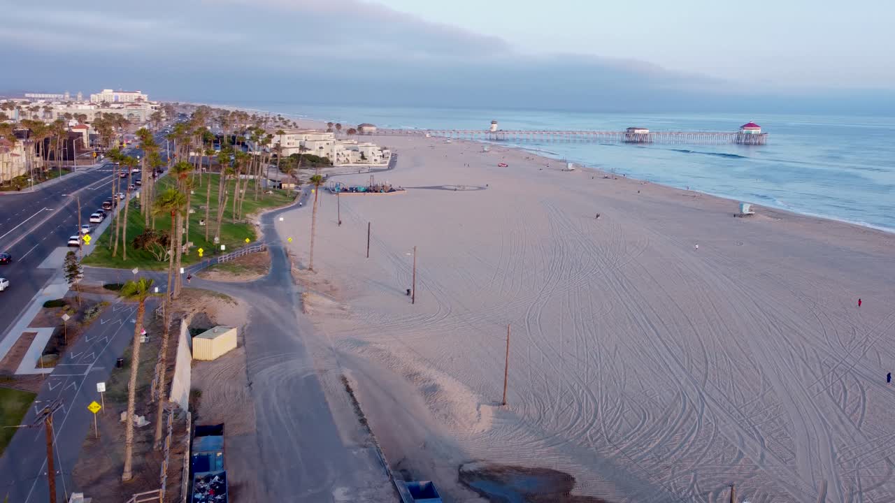 Muelle de Huntington Beach en la autopista Pacific Coast Highway 1. Coches circulando junto a palmeras tropicales al atardecer. Cálida luz dorada y tranquilas olas del océano. Condado de Orange, California