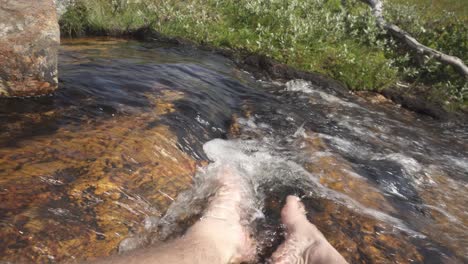 Male-hiker-dipping-feet-in-river-stream-running-water,-point-of-view-POV