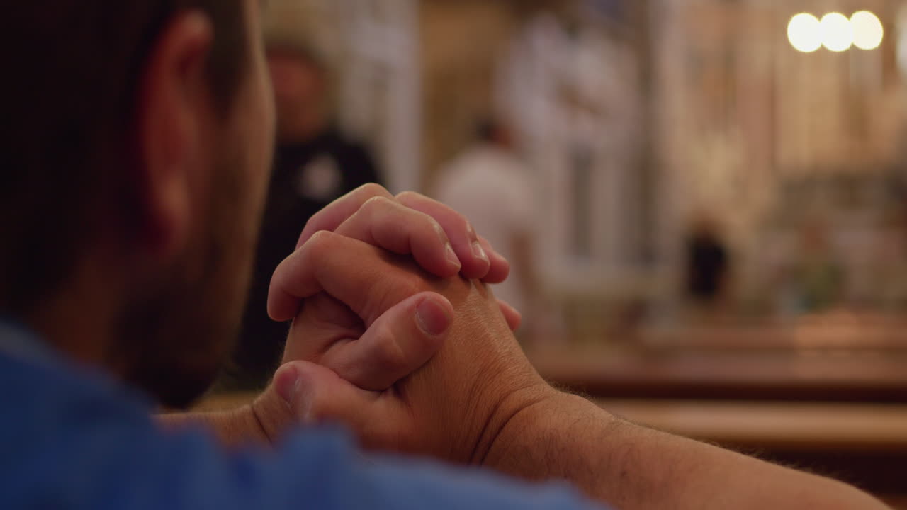 Man's Hands Clasped in Prayer Inside a Church