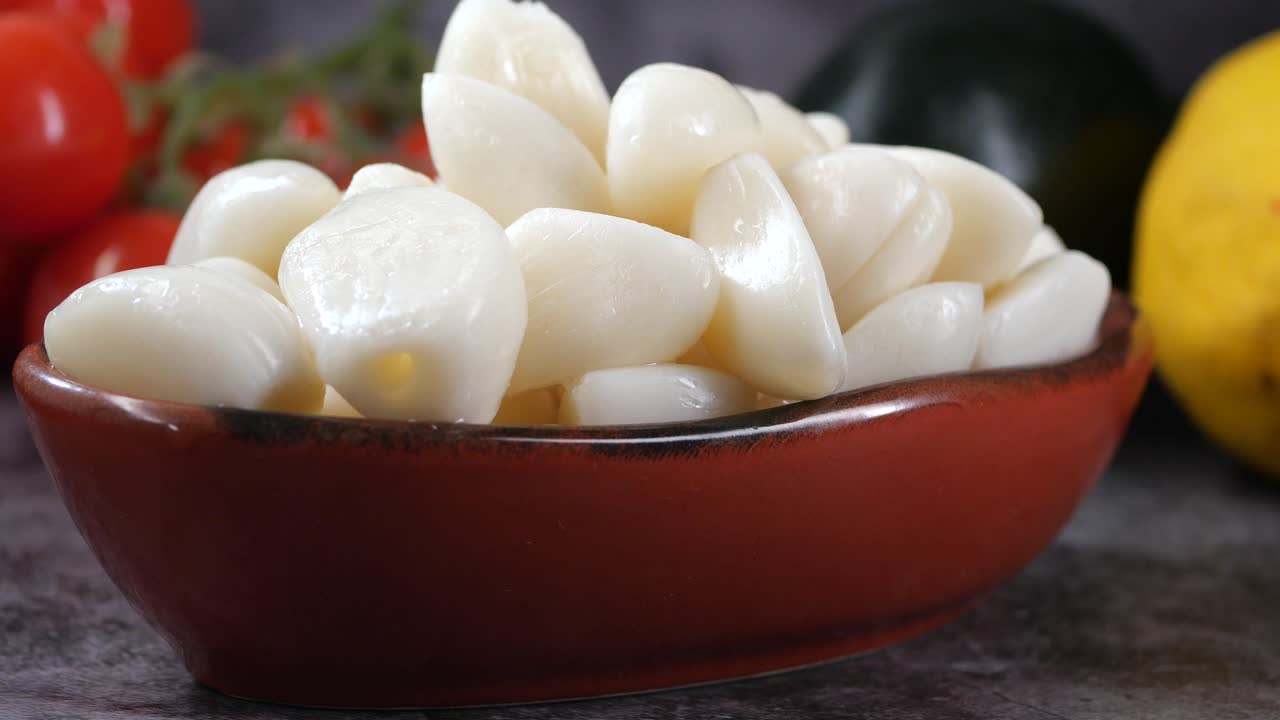 Spicchi d'aglio pelati in una ciotola con limone e pomodori
