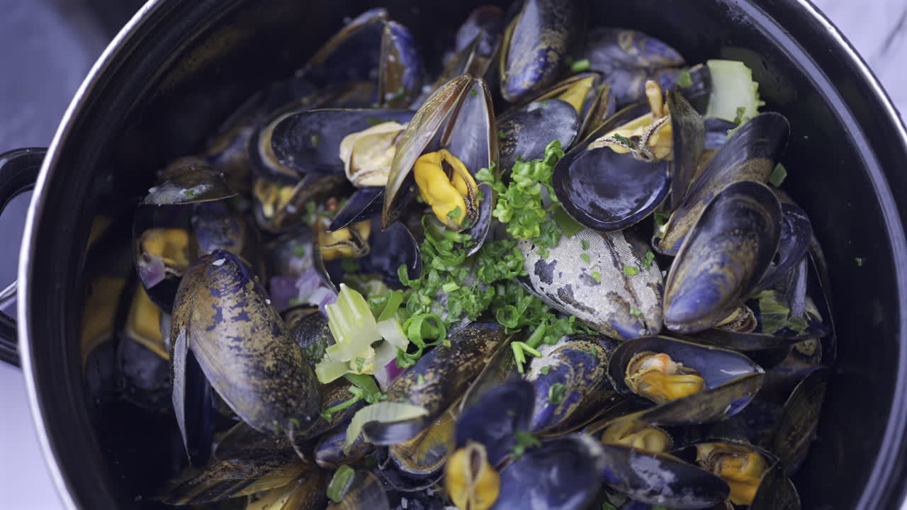 Close up of multiple steamy mussels in a pot with green onions on top
