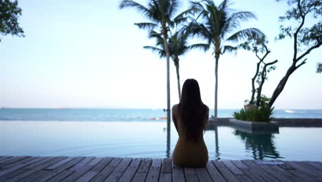 silhouetted woman sitting on wooden deck next to infinity pool looking out to the sea