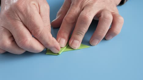 manos haciendo origami con papel verde