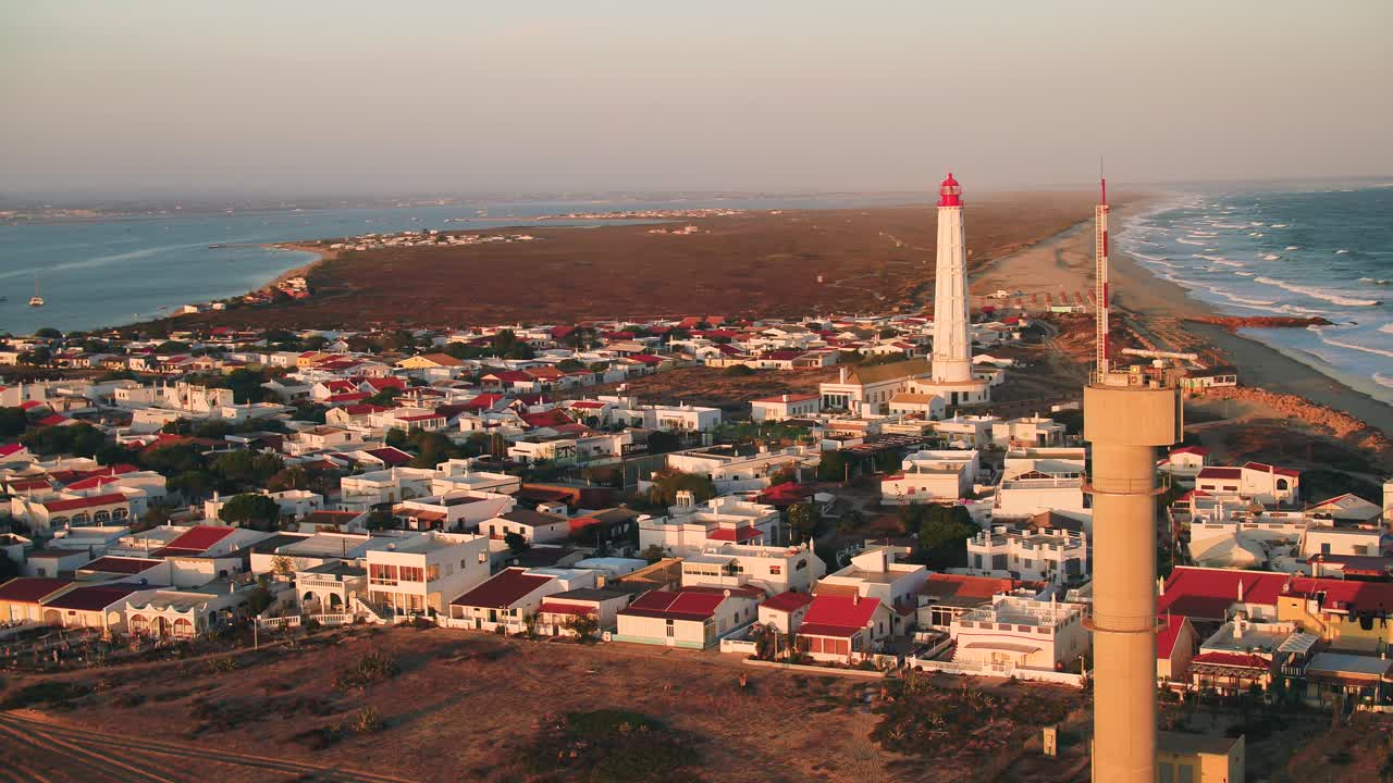 Ilha do farol. Panning aerial shot at sunset around the village, Cabo de santa maria lighthouse in the background