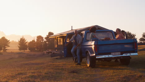 group of friends unloading backpacks from pick up truck on road trip to cabin in countryside