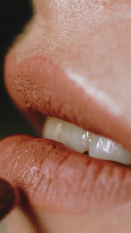 cu, slow motion: attractive young lady applies mate lipstick on lower lip with special brush on dark blurred background extreme close side view