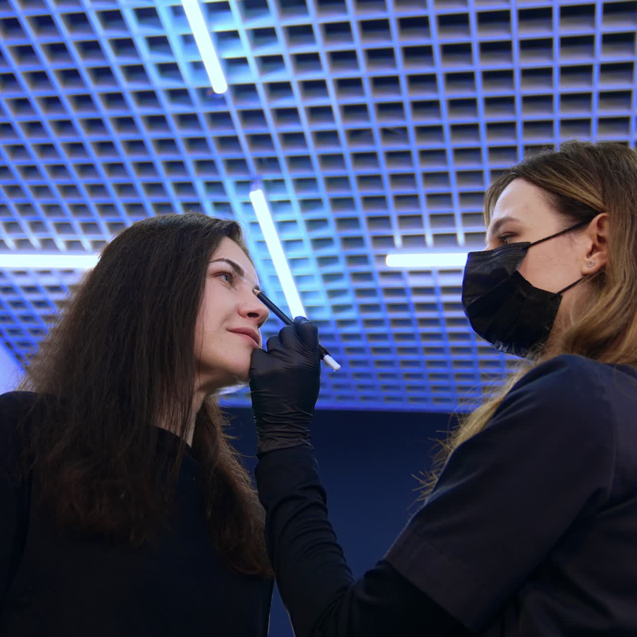 Beautician drawing white lines to mark the eyebrow limits. Brunette woman is prepared for the permanent eyebrow make up. Low angle view