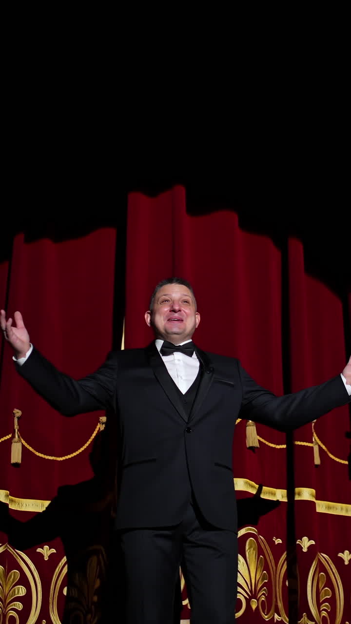 Theatrical stage. Man in costume appearing on a scene and presents the performance in light spot on dark background. Vertical video
