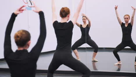 female students at performing arts school rehearsing ballet in dance studio reflected in mirror