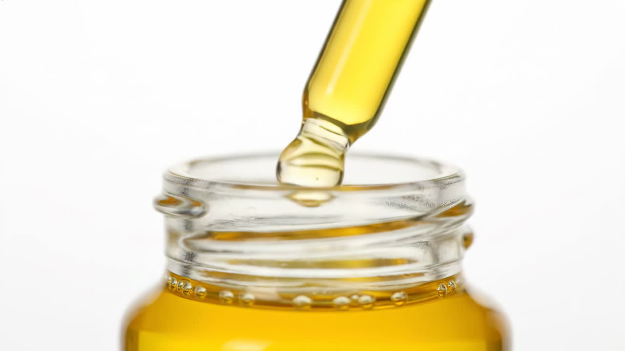Close-up of a dropper dispensing yellow liquid into a bottle