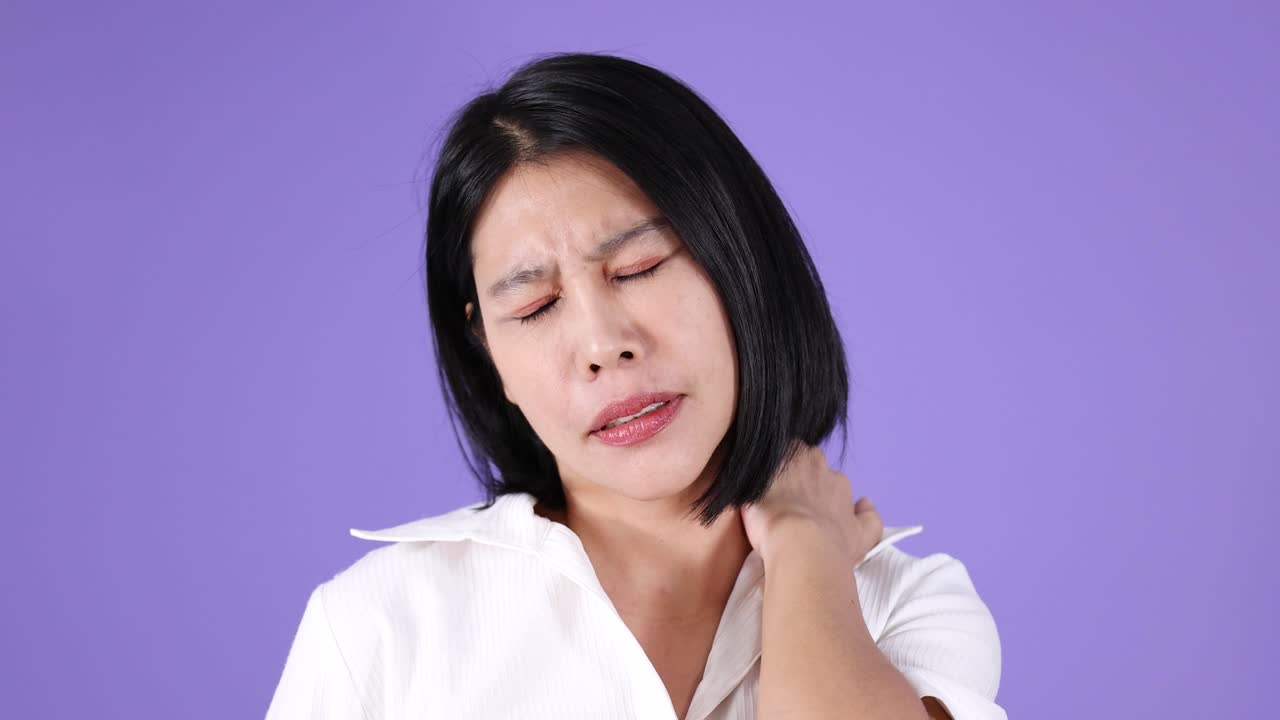 Asian woman in white shirt shows neck pain, discomfort, and fatigue under bright studio lighting