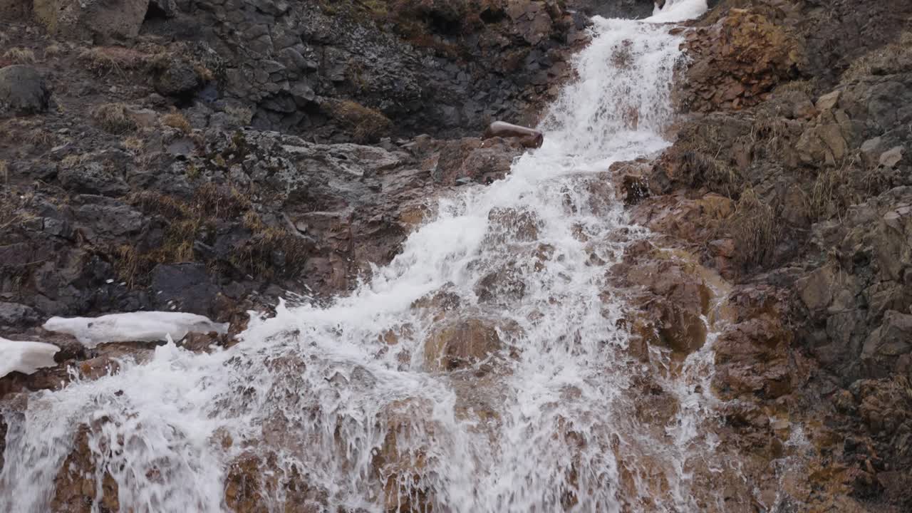 Piccola cascata a valle tra rocce nere e arancioni, Islanda