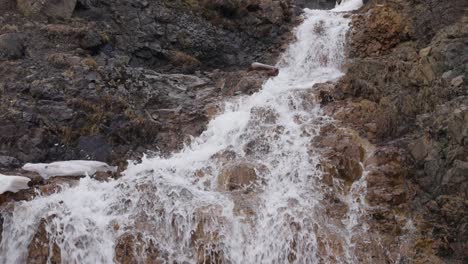 Kleiner-Wasserfall-Flussabwärts-Durch-Schwarze-Und-Orangefarbene-Felsen,-Island