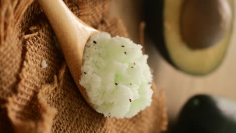 close-up of green body scrub on a wooden spoon with burlap and avocado