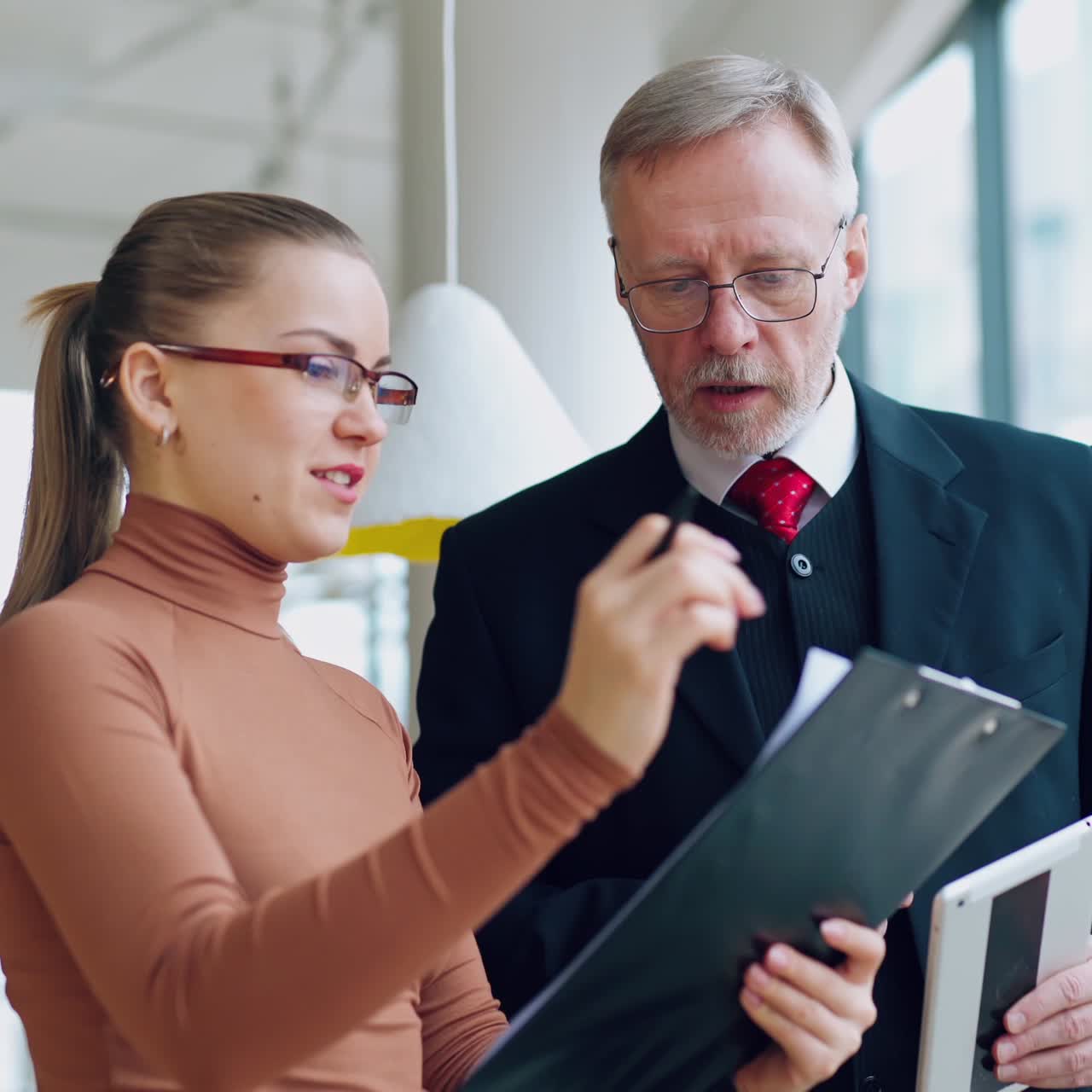 Smart secretary talks to her boss. Mature businessman in costume listening to the young woman showing documents in the office.