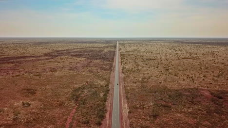 AERIAL-LOWERING---A-lone-car-travels-through-the-vast,-deserted-Australian-Outback