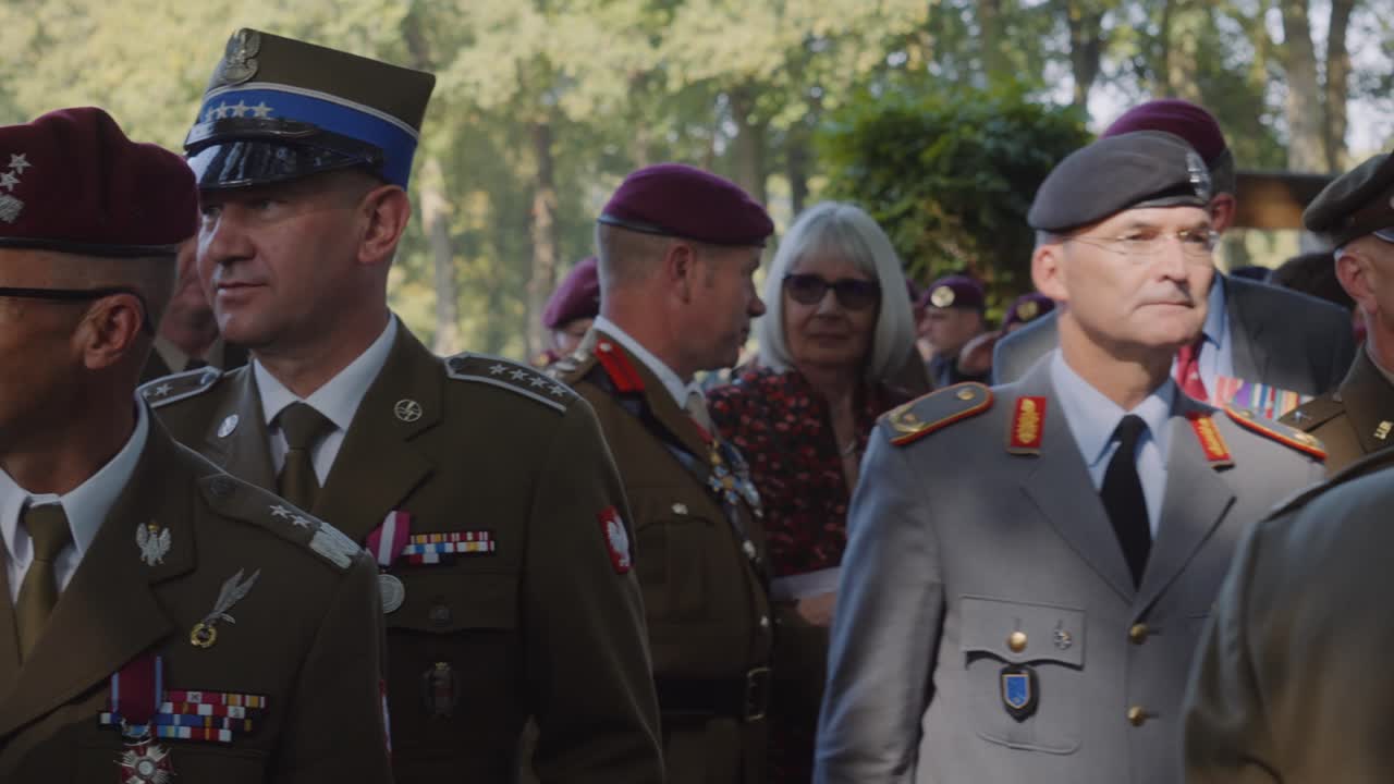 Polish military officers, dressed in full uniforms adorned with medals, march during a military commemoration ceremony. The officers proudly wear berets, showcasing their rank and achievements.