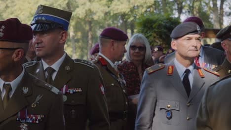 polish military officers, dressed in full uniforms adorned with medals, march during a military commemoration ceremony. the officers proudly wear berets, showcasing their rank and achievements.