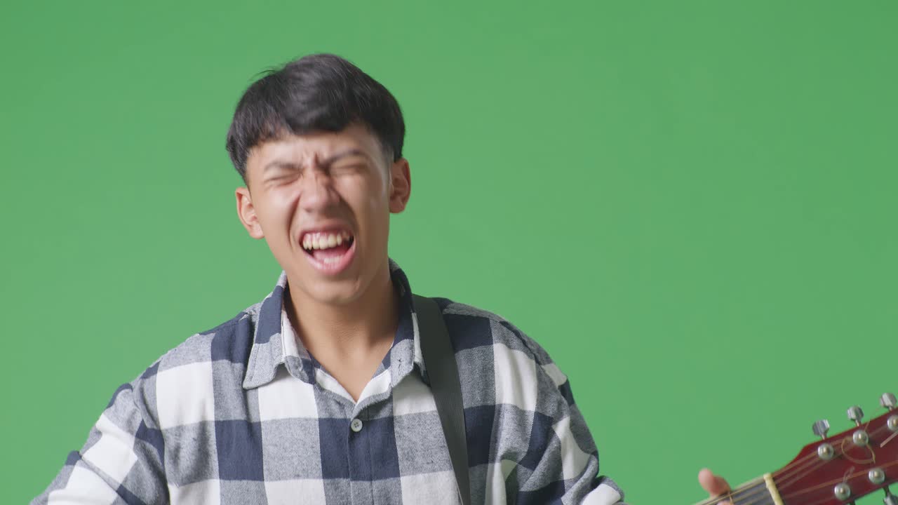 녹색 스크린 배경에 록 음악과 함께 기타를 연주하는 젊은 아시아 십대 소년의 클로즈업